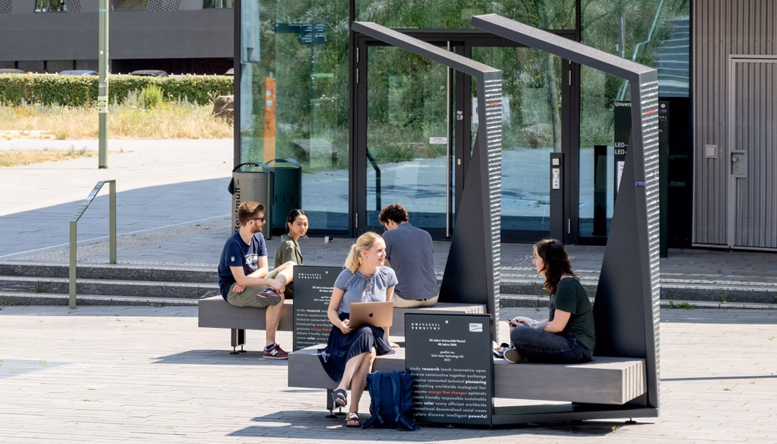 Students studying and collaborating outdoors at a Smart Shelter solar bench on a university campus