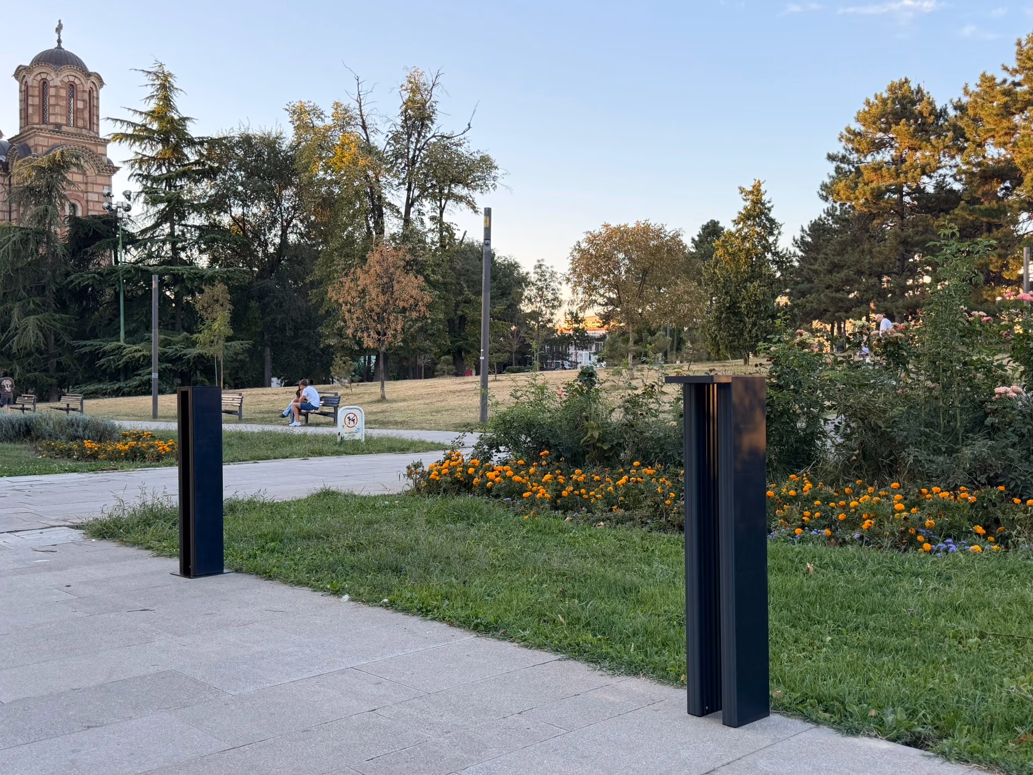 LED Bollard pair among flowerbeds at dusk, church in the background