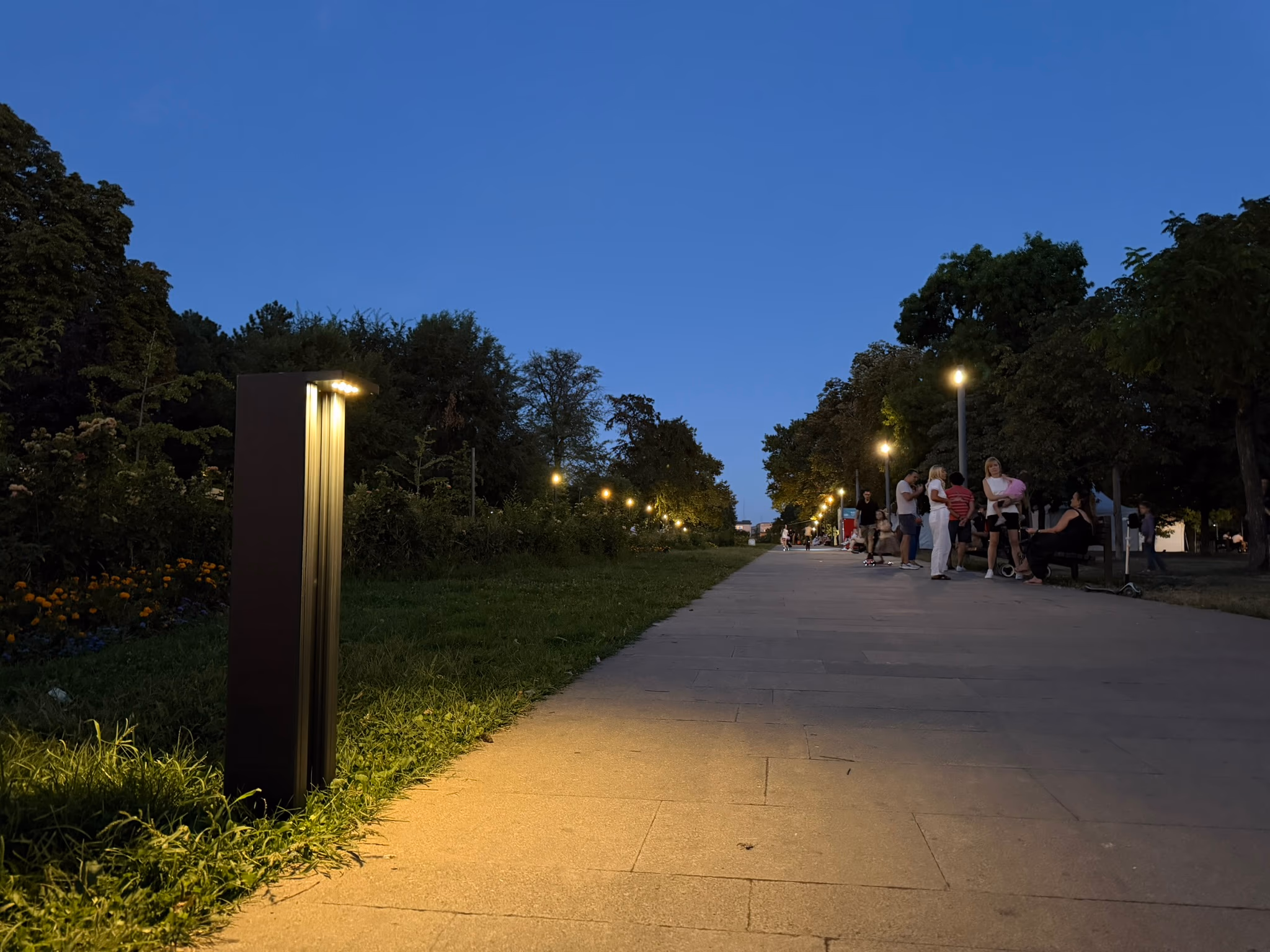 LED Bollard lighting a park path at dusk with people walking by