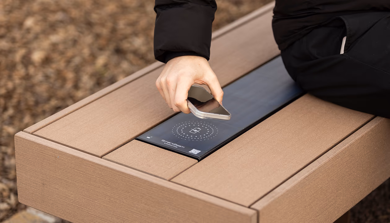 Hand placing phone on SmartBeam wireless charging bench outdoors